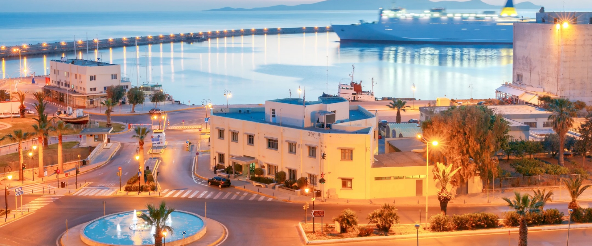 A panoramic view of Heraklion's historic Venetian harbor at sunrise, with the Koules Fortress prominently featured, fishing boats docked in the calm waters, and the sky displaying soft, warm colors.