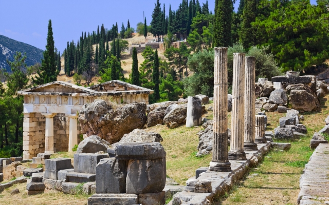 A panoramic view of the extensive archaeological site of ancient Delphi, Greece, showing the remains of the Temple of Apollo, the Treasury of the Athenians, the ancient theater, and the stadium, nestled on the slopes of Mount Parnassus.