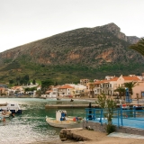 A view of the imposing fortified rock of Monemvasia rising dramatically from the sea, with the red-tiled roofs of the medieval town clinging to its hidden side.