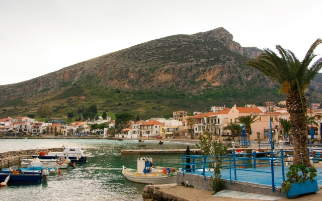 A view of the imposing fortified rock of Monemvasia rising dramatically from the sea, with the red-tiled roofs of the medieval town clinging to its hidden side.