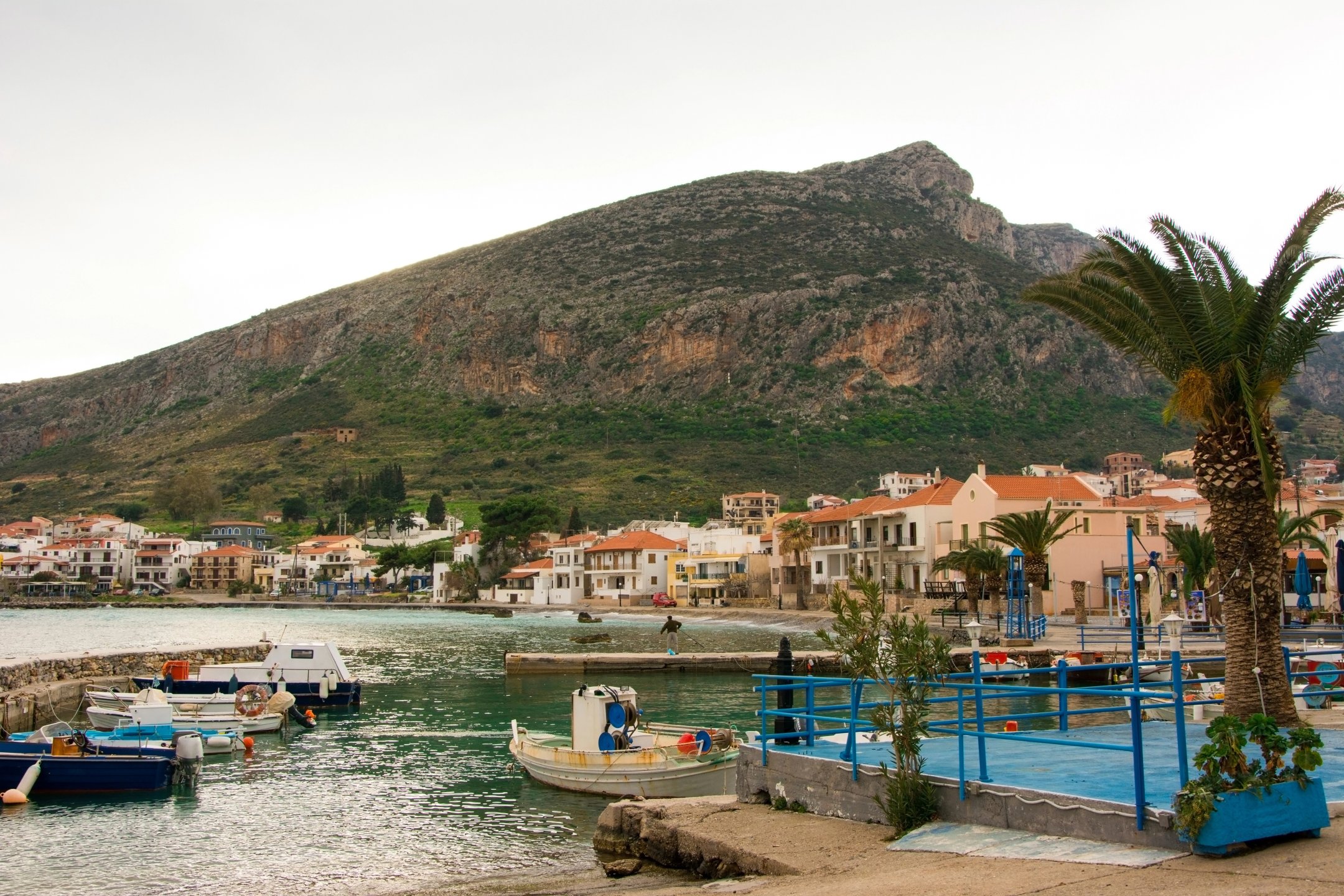 A view of the imposing fortified rock of Monemvasia rising dramatically from the sea, with the red-tiled roofs of the medieval town clinging to its hidden side.