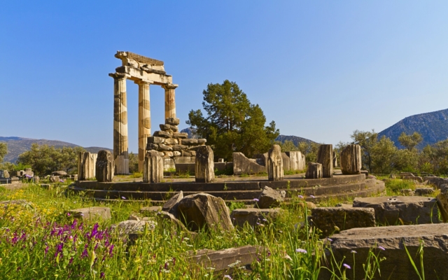 The distinct circular Tholos building at the Sanctuary of Athena Pronaia in Delphi, Greece, with its graceful reconstructed columns and circular base, nestled within ancient ruins and olive trees.