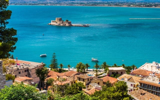 The small, picturesque Venetian fortress of Bourtzi, located on an islet in the harbor of Nafplio, Greece, with its stone walls rising from the calm blue sea under a clear sky.